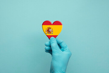 Hands wearing protective surgical gloves holding Spain flag heart