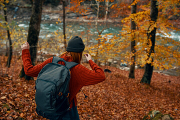 woman in a sweater with a backpack and in jeans walks through the autumn forest in the mountains near the river 