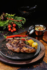 T-Bone steak serving with grilled vegetables on a black round plate on a background of greens, spices and vegetables, on a copper sheet. 