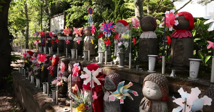 A slow motion of moving colorful windmills with Jizo statue daytime