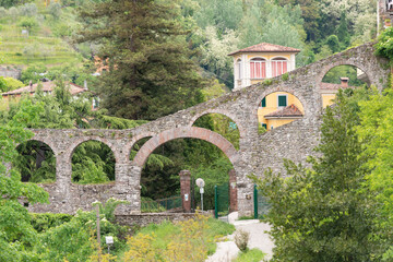 Fototapeta na wymiar Old aqueduct in the historic city. A stone aqueduct with arches descends from the mountains to the town of Barga.
