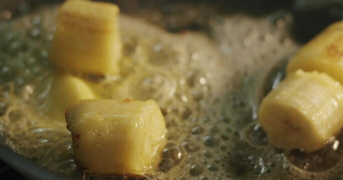 Cane brown sugar sprinkled on top of fried banana chunks in sizzling oil in a hot skillet