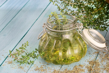 Thyme oil jar over a light blue wooden table with Thyme branches and powder around it