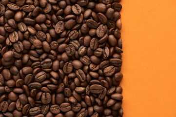 Roasted coffee beans on orange background with copy space. Close up top view.