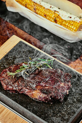 Fermented steak. Steak with rosemary on a black plate served with grilled corn on a background of greens, spices and fresh vegetables, on a copper sheet