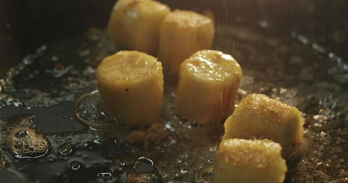 Cook sprinkles banana slices in oil with cane sugar on a hot skillet