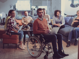 Fototapeta premium Disabled businessman in a wheelchair at work in modern open space coworking office with team