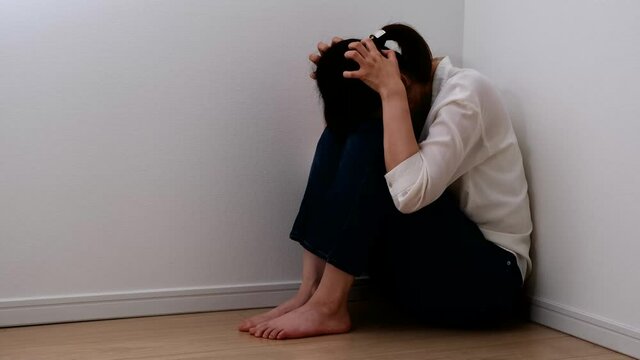 部屋の片隅で不安に押しつぶされそうになる女性