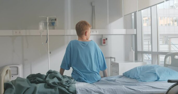Back view of kid patient sitting on hospital bed looking out of window