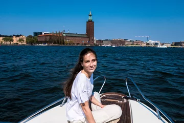 Foto op Canvas Stockholm, Sweden A young woman sits on the bow of a motorboat with the CIty Hall in the background. © Alexander