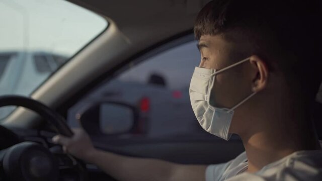 young asian male driver wear protective face mask while driving inside the car, protect self from pandemic, new normal life, city traffic jam, covid19 illness infectious diseases prevention, side view