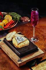 Grilled Camembert Cheese on a black square stone plate with toast and grilled vegetables on a copper background.