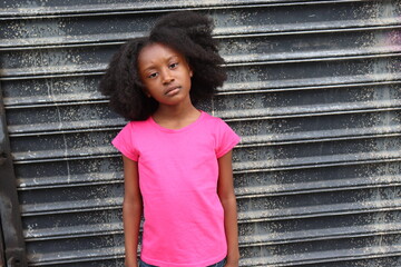 Young Black Girl with natural hair afro Standing outdoors with serious face  wearing pink shirt