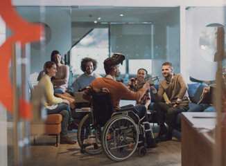 Disabled businessman in a wheelchair at work in modern open space coworking office with team using...