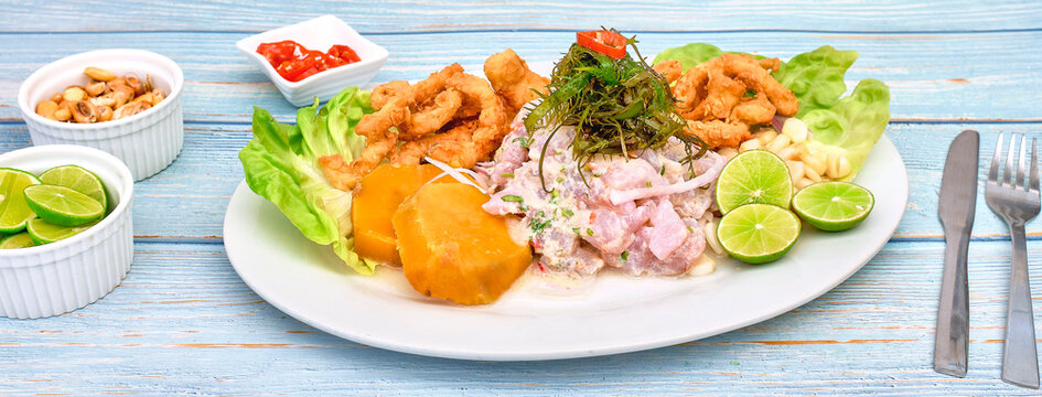 Peruvian food: fish ceviche and chicharron de pescado with fried cassava, sweet corn and sweet potato, served on a white plate