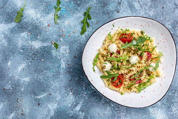 Fusilli Pasta Caprese salad with tomato, mozzarella vegetable paste on a blue background, fresh, salad, banner, menu, recipe. Healthy food