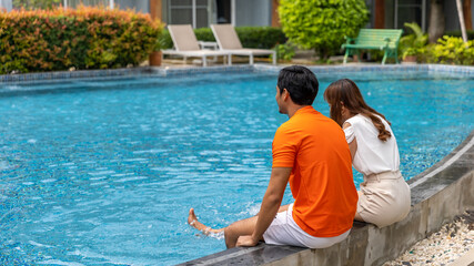 Young couple spends time together for vacation at a swimming pool in a garden resort. A married couple sit and relax at a swimming pool during a beautiful holiday