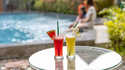 Foreground focus of colorful cocktail or refreshment drinks on a glass table with background blurred of a lovely family on a swimming pool in resort during holiday