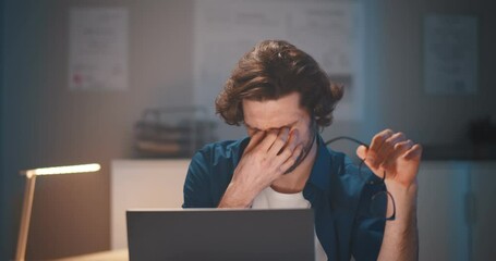 Young businessman having headache working overtime with laptop at office late night.