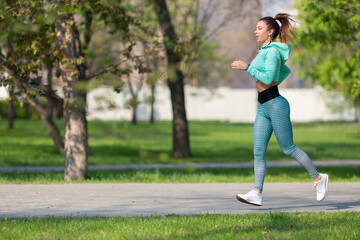 Full length photo of a woman running in park in early morning. Attractive looking woman keeping fit and healthy.