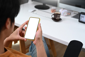 Over shoulder view of young man sitting at office desk and using smart phone.