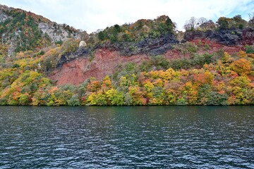 遊覧船から見た赤茶けた岩肌とカラフルな紅葉のコラボ情景＠青森