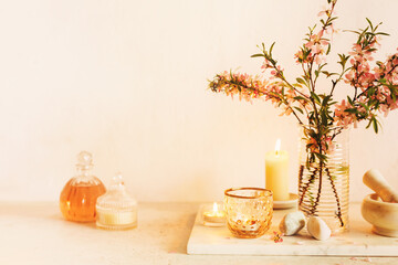 Scented candles, essential oils, marble mortar and wild almonds flowers on a table. Spa concept. Toned image.