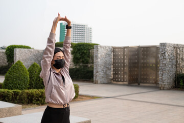 Selective focus at face of young beautiful Asian women wearing surgical face mask while stretching warm up before exercise or running at the park in the morning. New normal lifestyle.