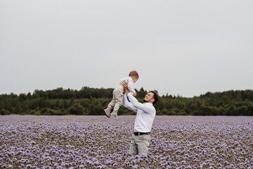 The father picked up his son in his arms and plays with him in a blooming field