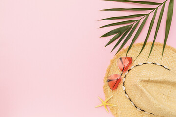 Ladies straw hat, sunglasses and palm leaf on pink background with copy space, summer background