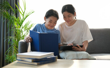 Obraz premium Two young asian girls sitting on sofa and using digital tablet together.