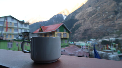 Morning cup of tea with mountain village background at sunrise.