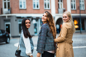 Portrait of three women standing on street and looking at camera. Girlfriends in the city.