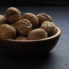 Walnuts in a wooden bowl on a dark background.