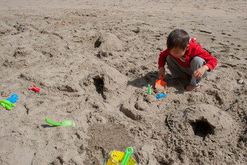 Little boy playing with the sand and sand toys at the beach. Boy building roads and tunnels with the sand. Pacific ocean. Outdoor summer activity. Horizontal, copy space.