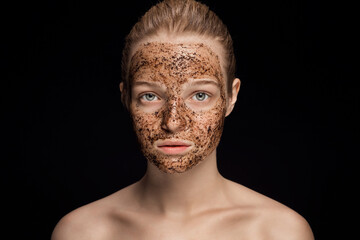 Skin scrub Coffee grounds mask on the face of a beautiful young woman Organic natural cosmetology dark studio background Isolate