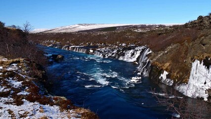 Beautiful view of popular Hraunfossar cascades (Icelandic: lava waterfalls) near Húsafell in western Iceland on sunny winter day with wild river, ice formations and turquoise colored water. - Powered by Adobe