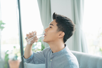 Single man drinking water from a glass sitting on a couch at home - 433746637