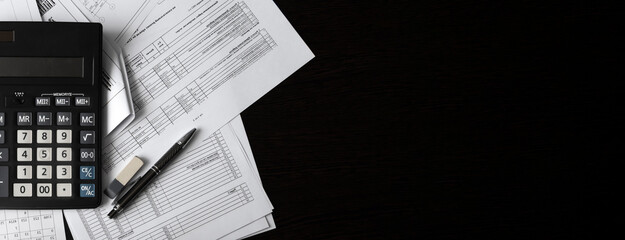 A business banner with working documentation, a large black calculator, and a pen on a dark wooden table. The design element of the header of the website about education in the field of finance.