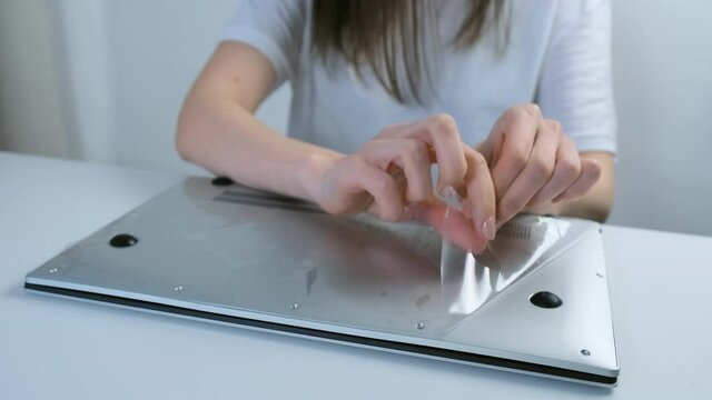 A woman's hand removes the film from a new laptop of silver color, closeup view. Buying a computer and unpacking it. The concept of gadgets and computers.