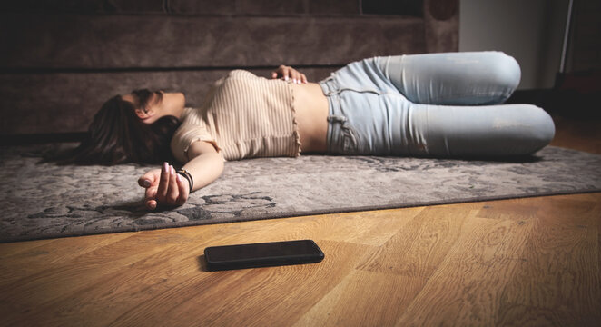 Unconscious young woman lying at home. Smartphone on the floor