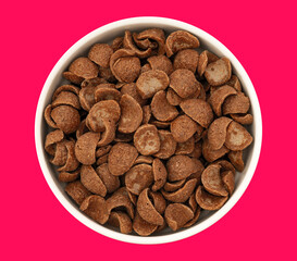 Top view of bowl with sweet chocolate cereal flakes for breakfast on red background