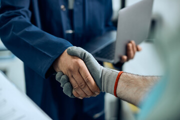 Close-up of auto repair manager and mechanic shaking hands in a workshop.