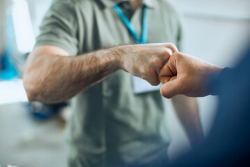 Close-up of auto repairmen greeting with fists at car workshop.