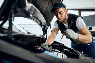 Young mechanic checking oil level of car engine at repair workshop.