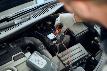 Close-up of mechanic attaching jumper cables on car engine while working at repair shop