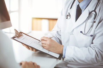 Unknown male doctor and patient woman discussing current health examination while sitting in sunny...