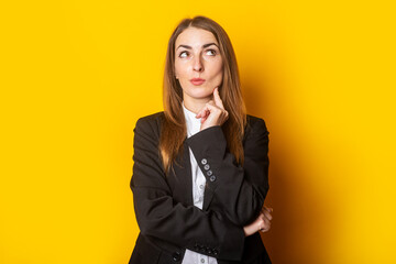 pensive young business woman lady in black jacket looks up on yellow background