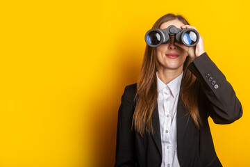 young business woman looking through binoculars on a yellow background - obrazy, fototapety, plakaty