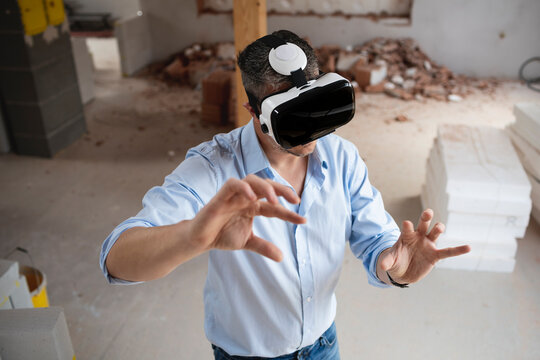 good looking male architect with virtual reality goggles and blue shirt on construction site in loft, attic